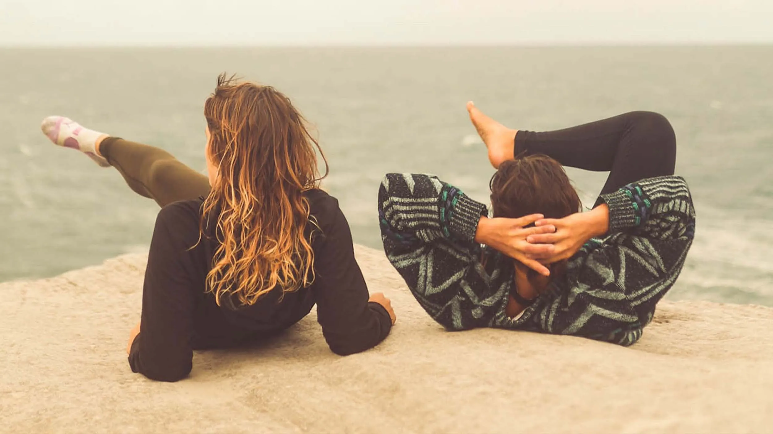 tess and a friend stretching on a sandstone ledge above a misty sea