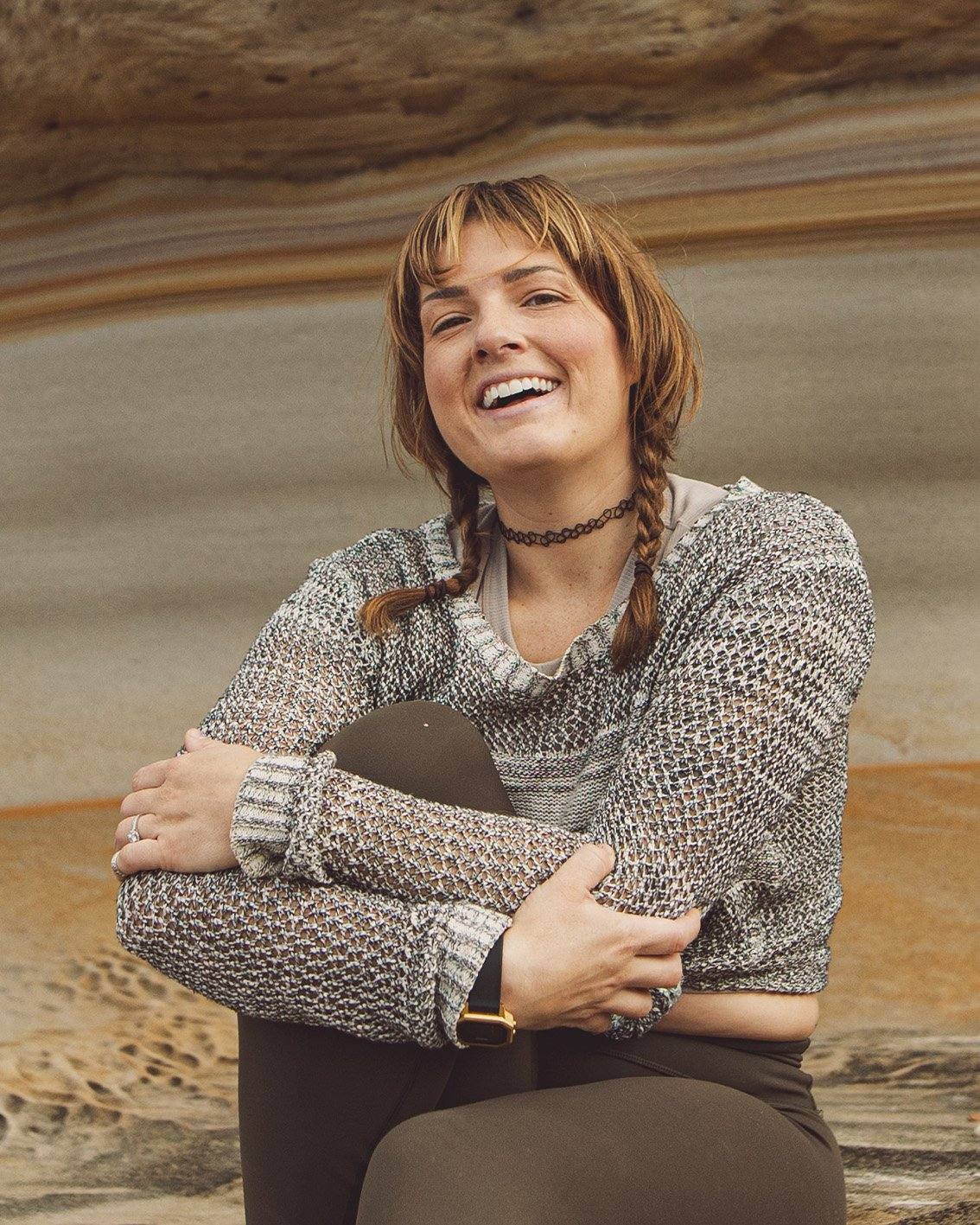 tess laughing, hugging one knee in front of a layered sandstone wall